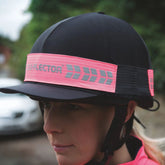 Person wearing a riding helmet with a pink reflective band outdoors